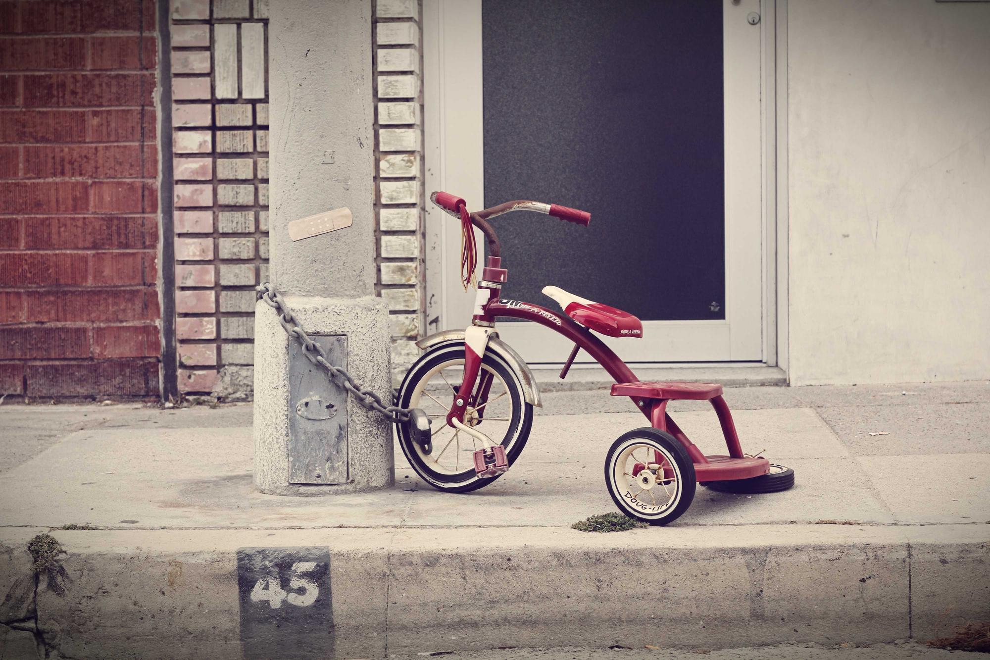 A small red tricycle chained beside a doorway