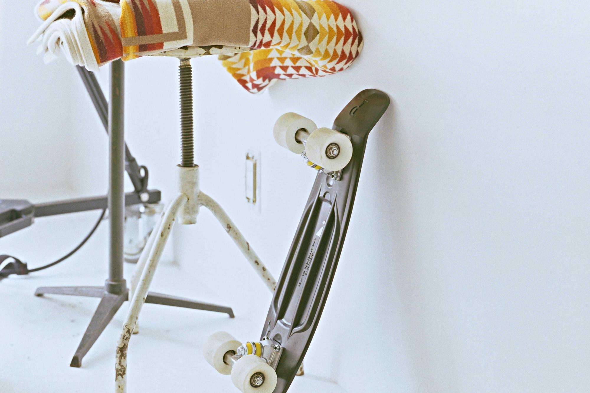 A white skateboard leaning beside a metal stool against a white wall
