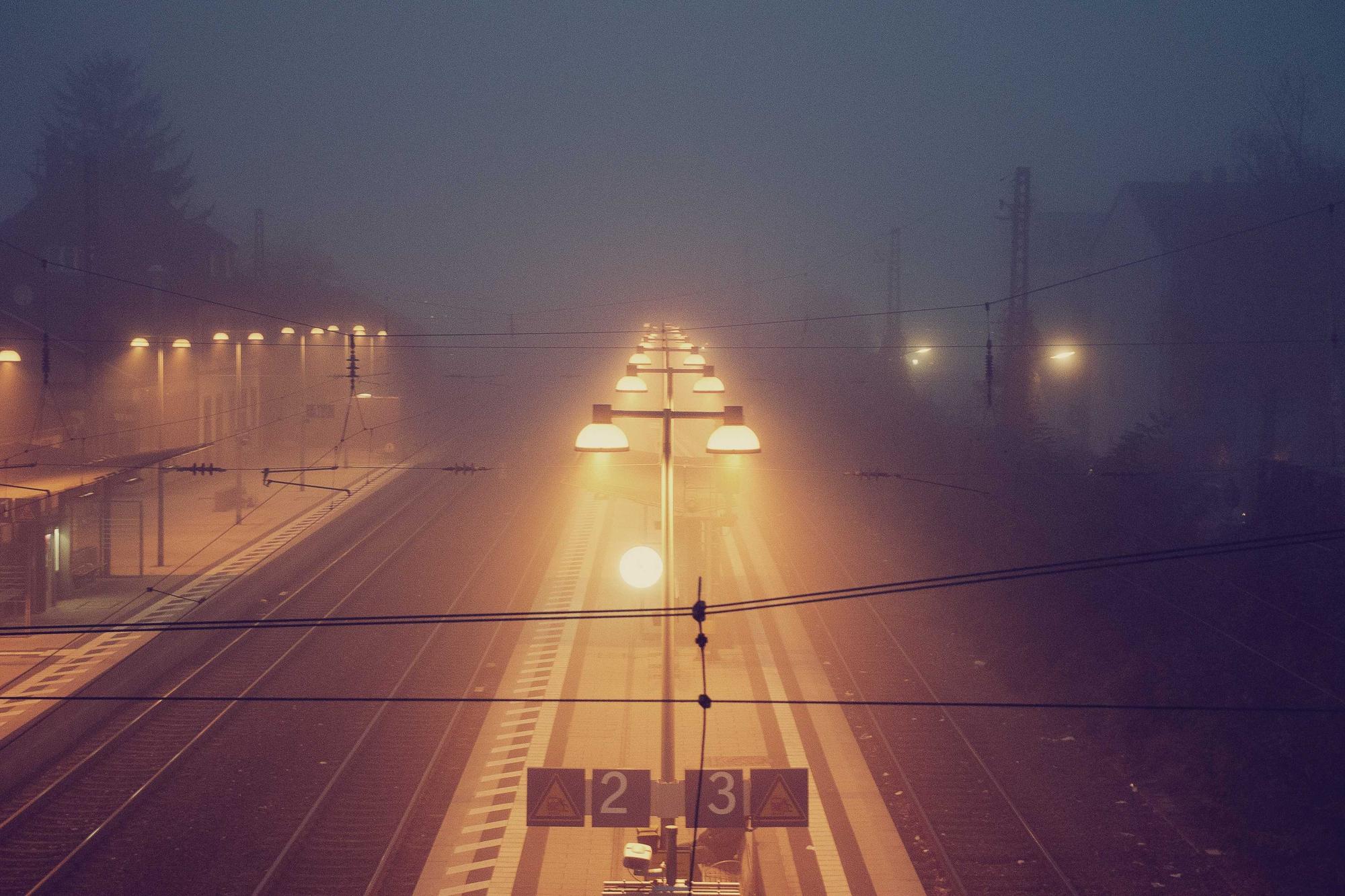 A quiet railway platform in evening fog with lamps glowing along the track