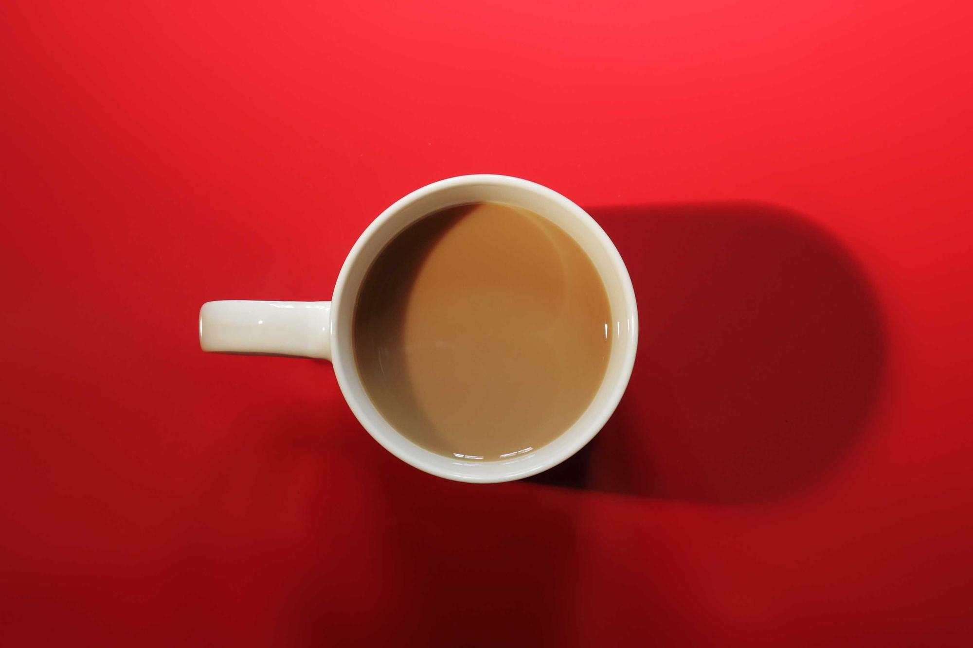 A white cup of coffee seen from above on a saturated red table